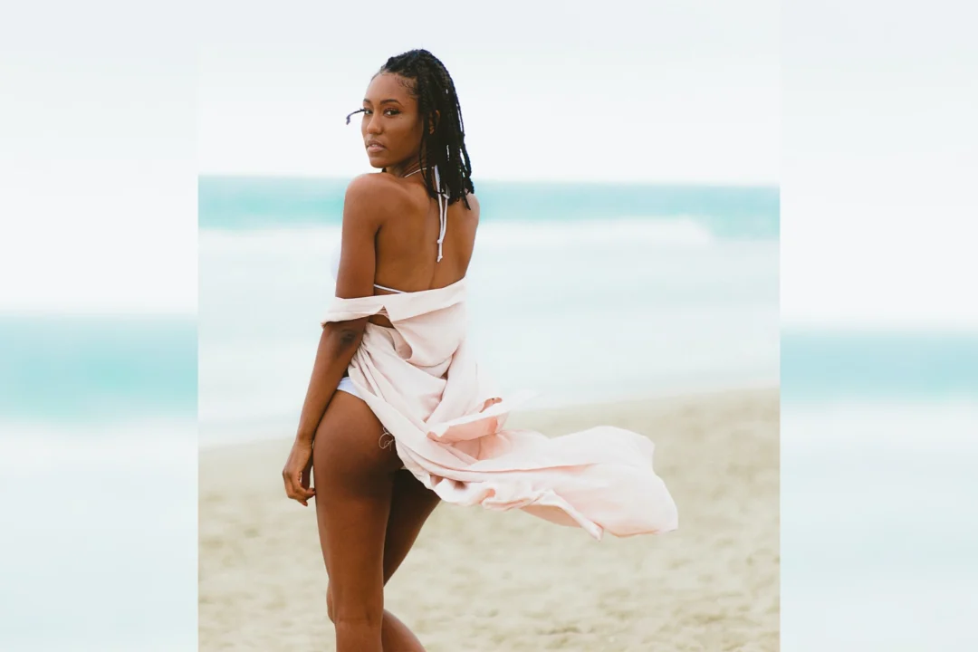 Woman in a flowing dress standing on a beach with ocean in background.